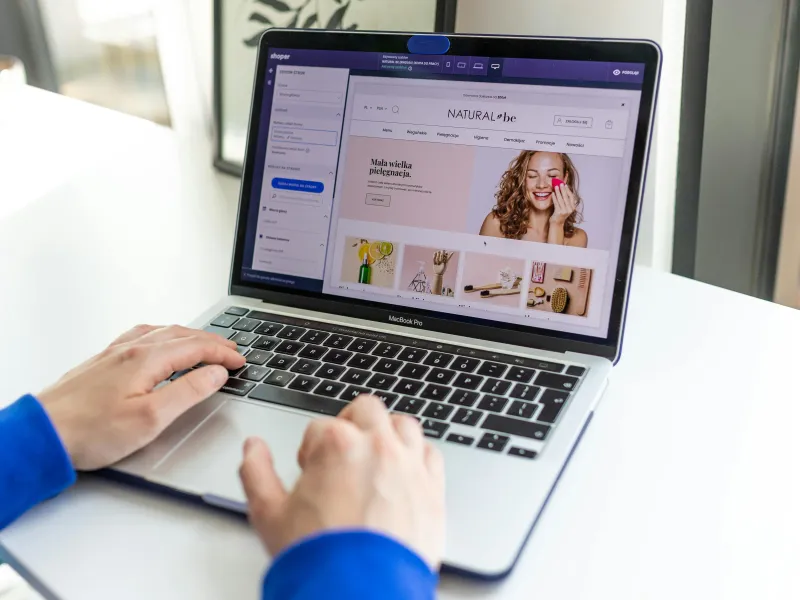 Person using a laptop to manage an online store's website, showcasing product images and website editor tools.